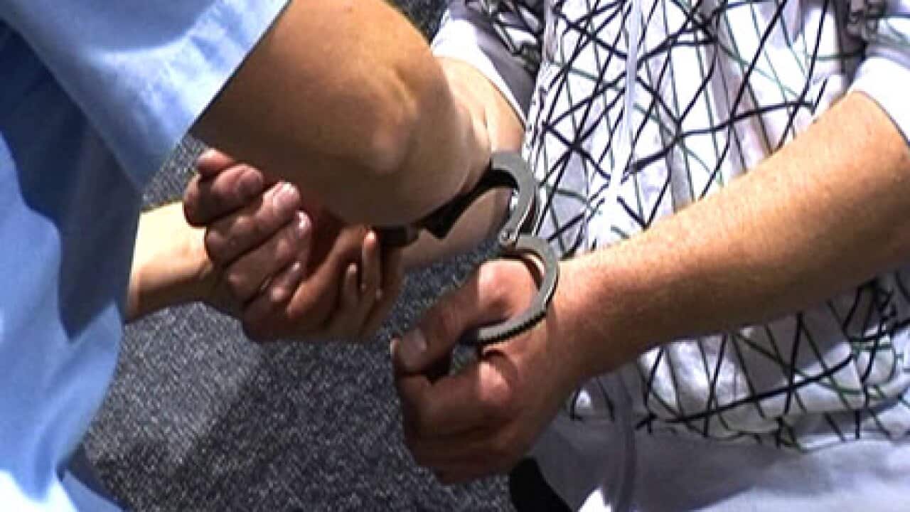 A close up picture of the wrists of a man being handcuffed.