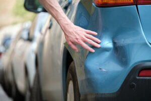A close-up of a blue car's rear bumper showing a dent and scratches.