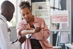 A woman shows her arm to a doctor in an office. The doctor is taking notes on a tablet.